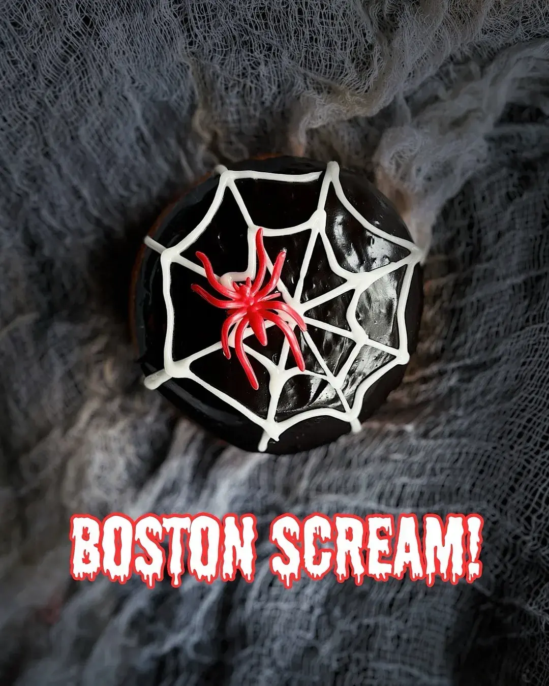 black doughnut with red plastic spider on top and the words “boston scream!” across the bottom.