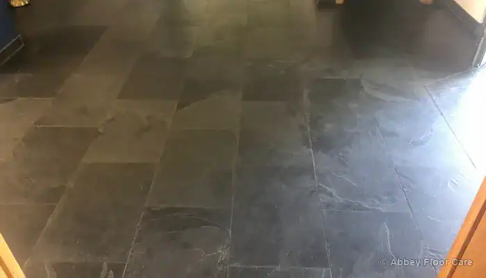 Thick buildup of discolored floor wax along slate tile edges and grout